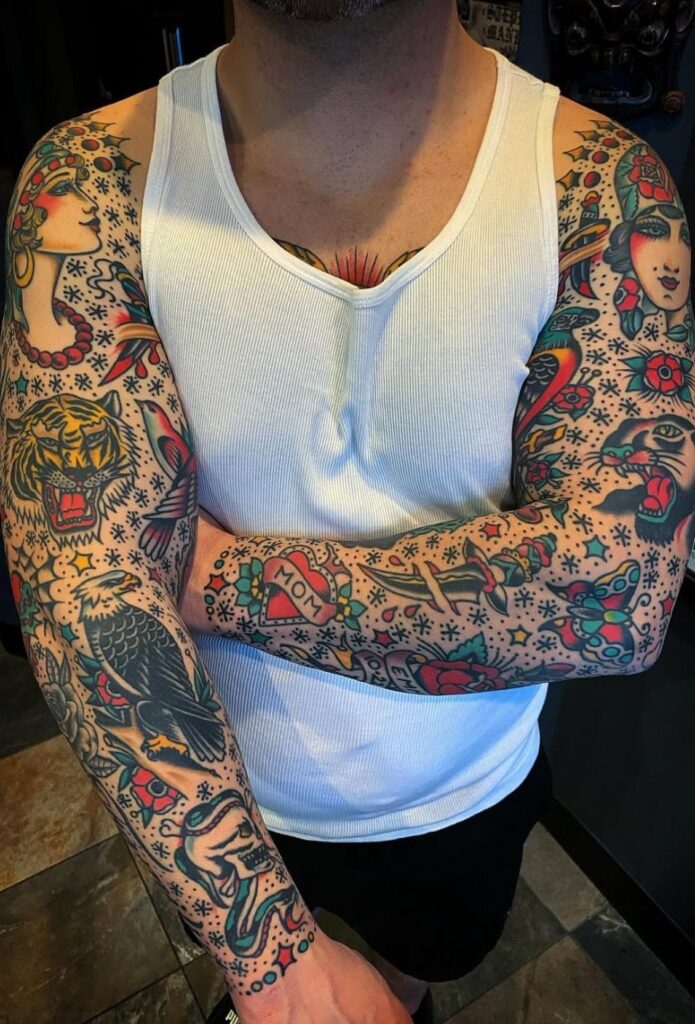Full American traditional tattoo sleeves on a person wearing a white tank top.