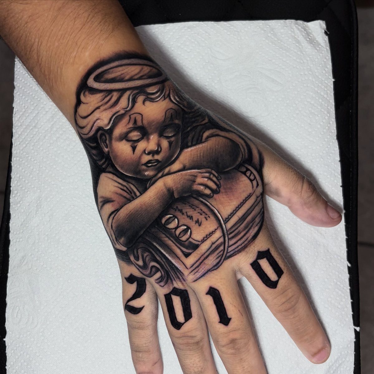 Angel cherub tattoo on a hand with the year 2010 on knuckles