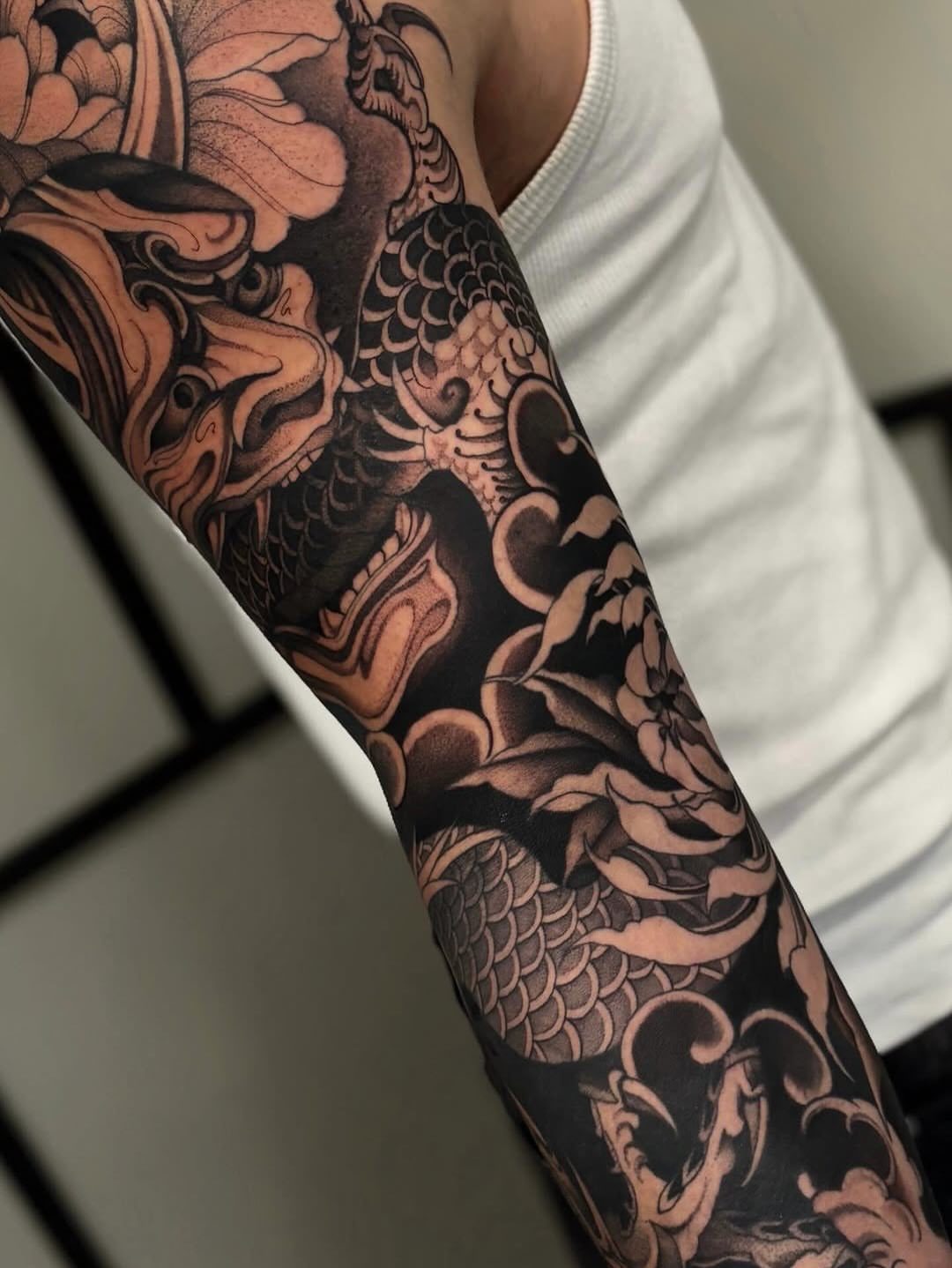 Japanese style dragon and flower tattoo covering a person's arm in black ink