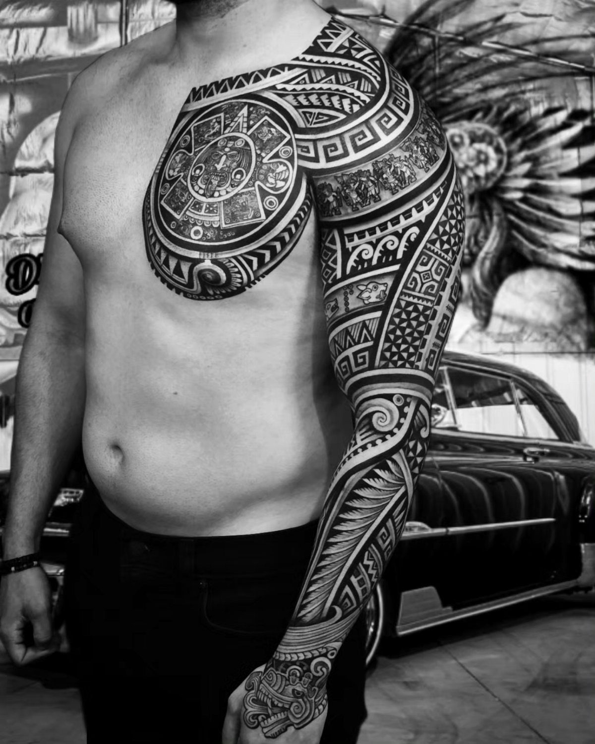 Man with geometric aztec pattern tattoos on his chest and full left arm