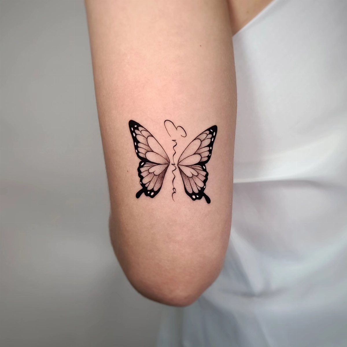 Butterfly tattoo on an arm with a name forming the butterfly's body.