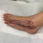 Calligraphy tattoo in black ink on the top of a foot with pink toenails