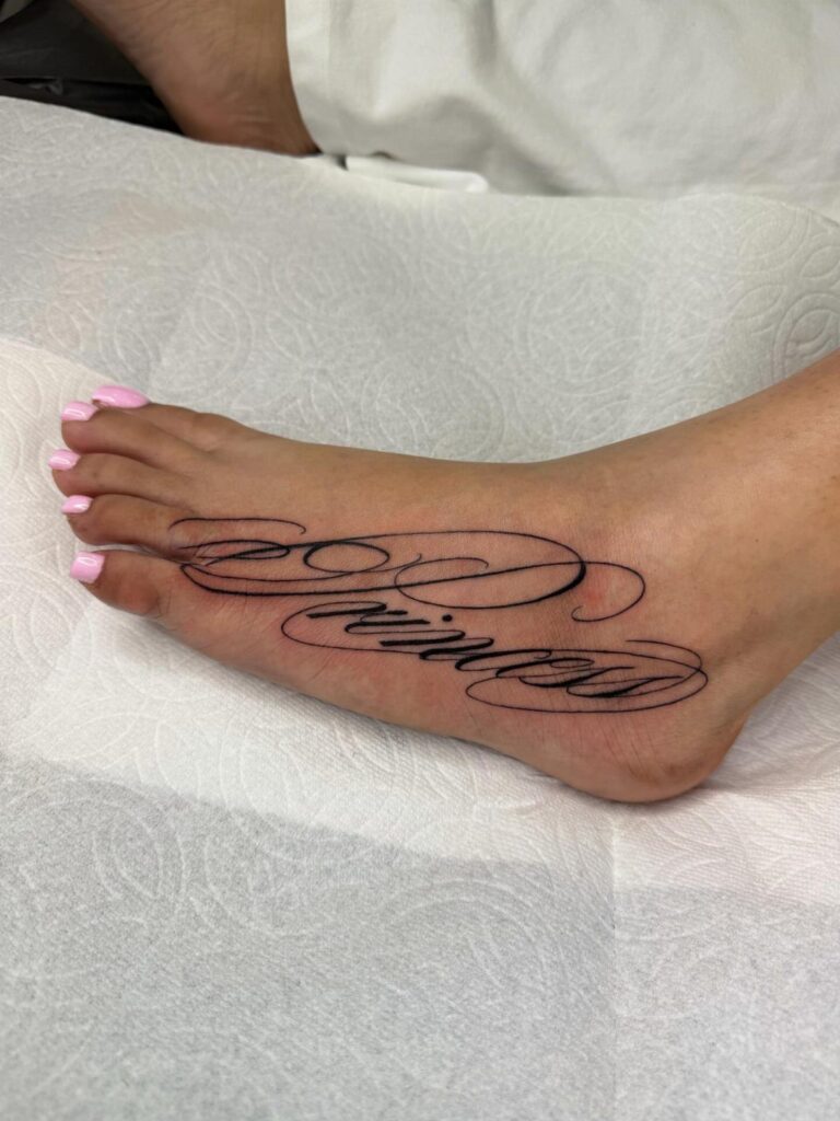 Calligraphy tattoo in black ink on the top of a foot with pink toenails