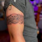 Celtic knot tattoo band wrapped around a person's upper arm in black ink.