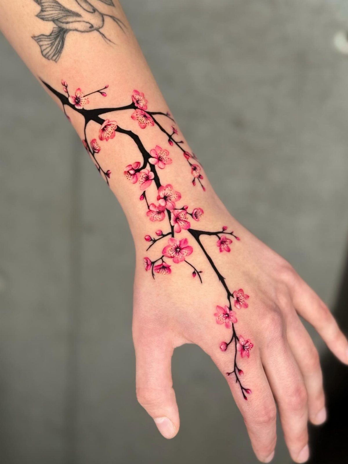 Cherry blossom branch tattoo with pink flowers on a person's forearm and hand