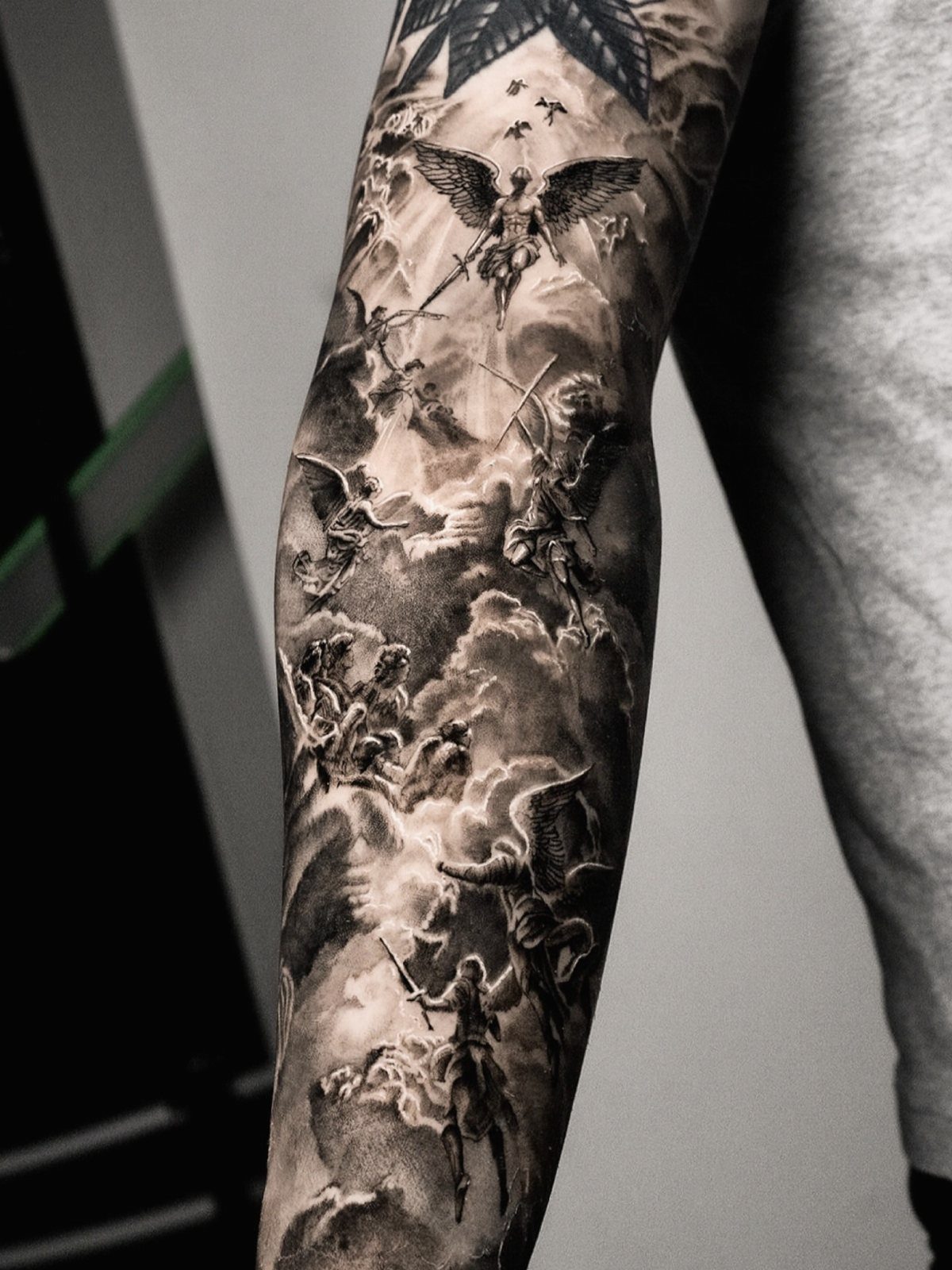 Detailed black and grey sleeve tattoo featuring angels and religious figures among clouds.