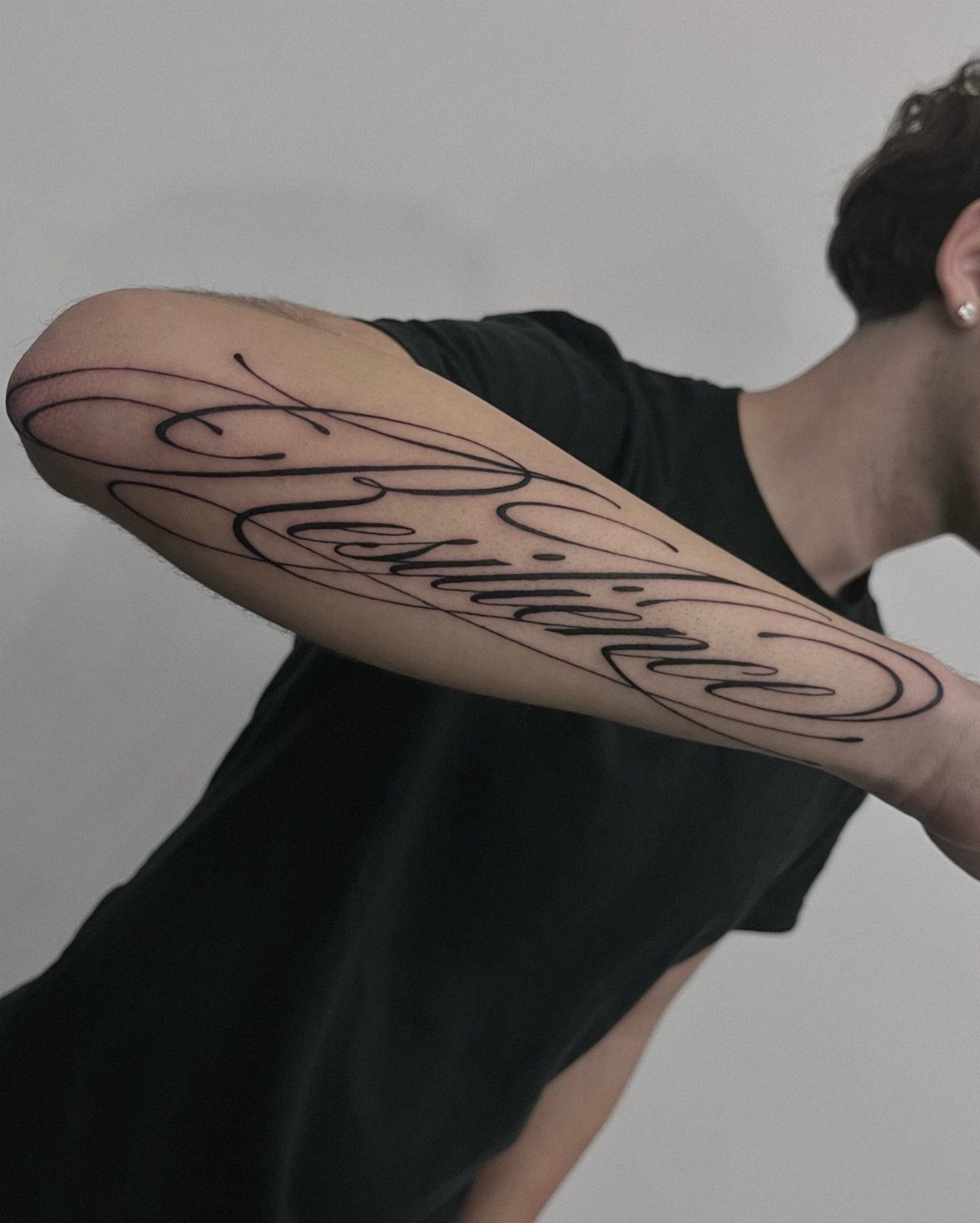 Cursive lettering tattoo of the word Resilience on a person's forearm