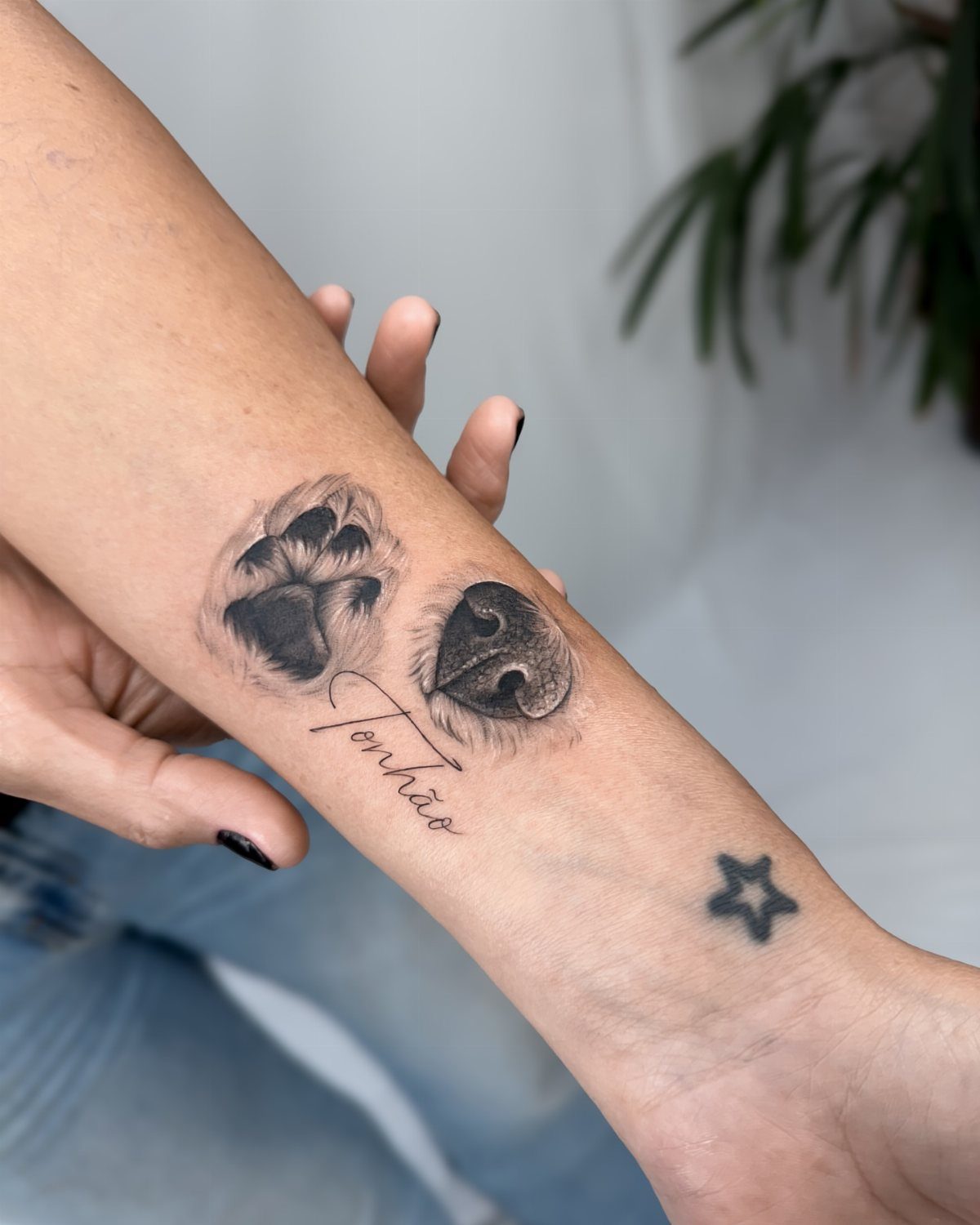 Dog paw and nose tattoos with the name Tonhão on a person's forearm.