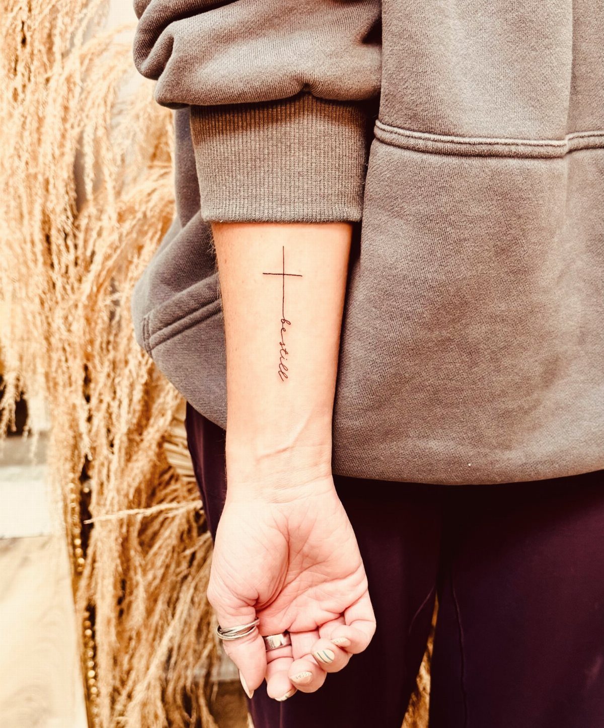 Small black cross tattoo with the word faith on a person's inner wrist