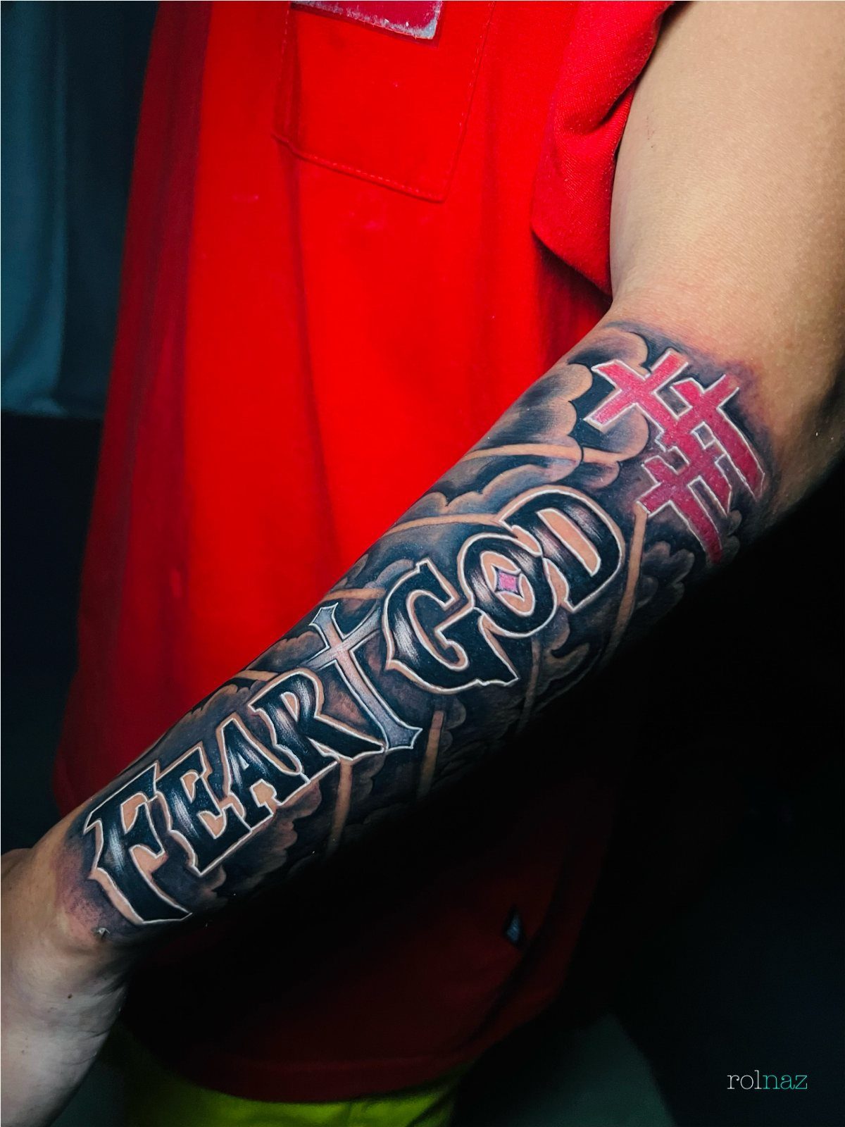 Forearm tattoo with 'FEAR GOD' text, grey clouds, and red crosses.