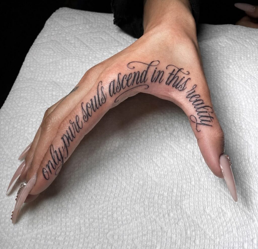 Cursive script tattoo on a hand reading only pure souls ascend in this reality