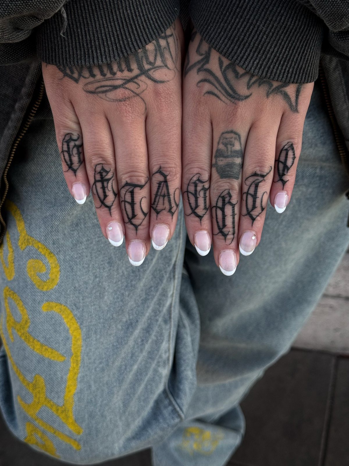 Hands with gothic word tattoos on knuckles and white French tip nails