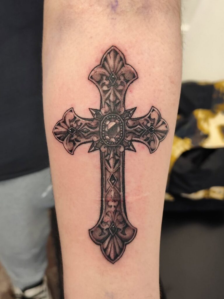 Ornate filigree cross tattoo with intricate gothic patterns on a person's forearm.