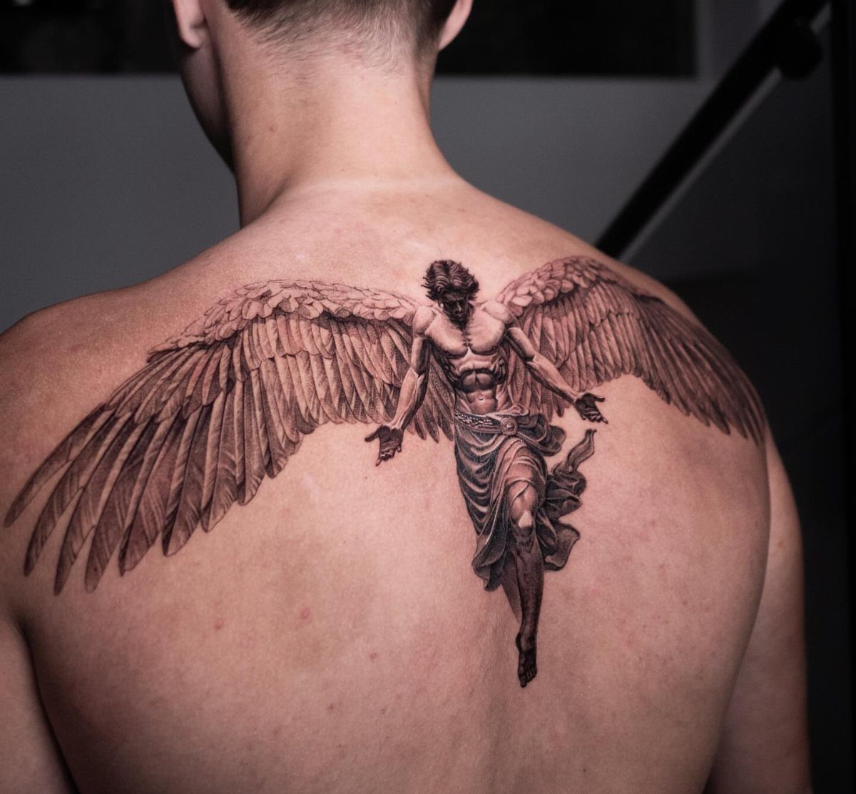 Detailed black and grey angel tattoo with large wings on a man's back