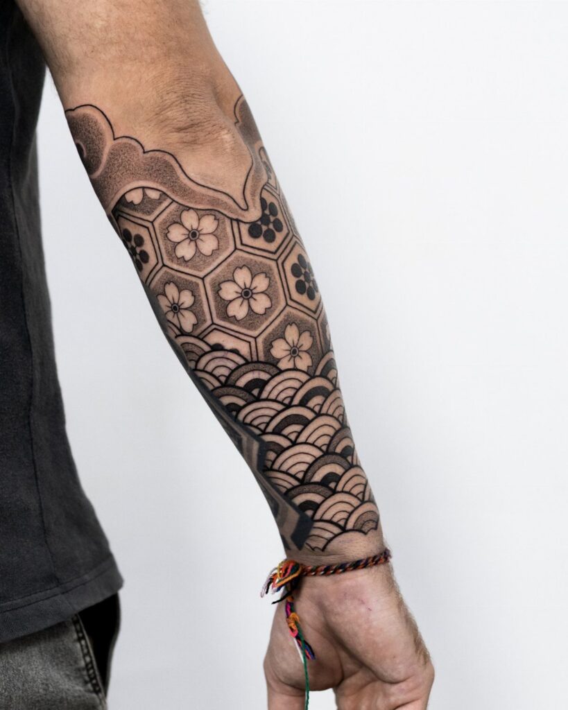 Forearm with a black ink Japanese tattoo featuring cherry blossoms and wave patterns.