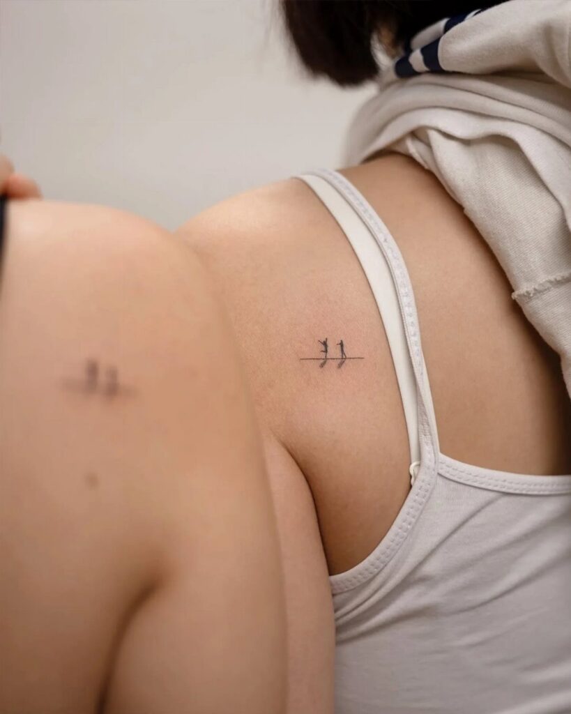 Two people showing matching small bird tattoos on their upper backs.