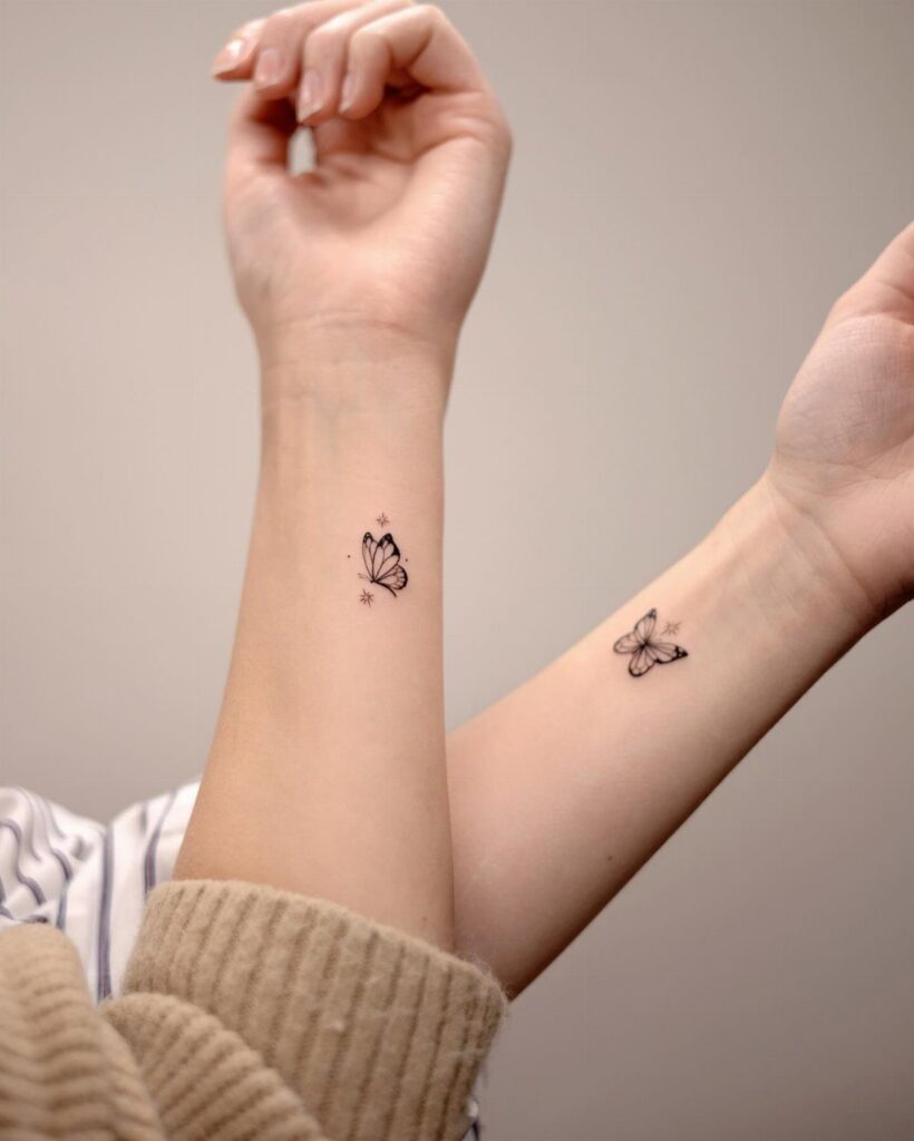 Two matching small black butterfly tattoos on the inner wrists of two people.