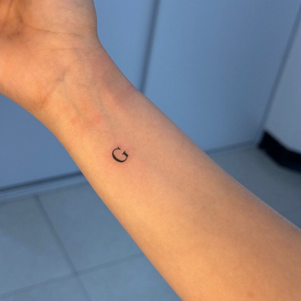 Small black letter G tattoo on the inner wrist of a person