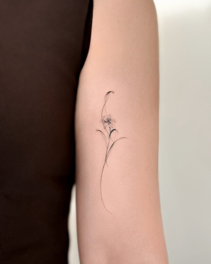 Fine line flower tattoo with a delicate stem on a person's upper arm.