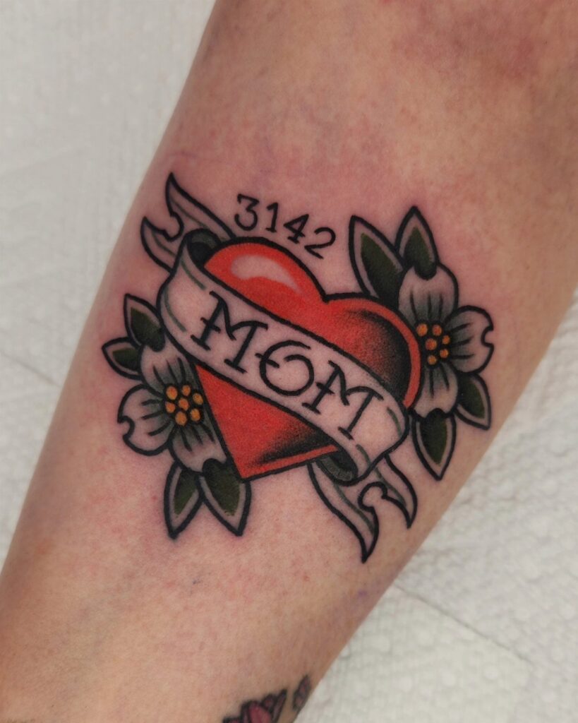 Traditional red heart tattoo with MOM banner and flowers on a forearm