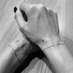 Two wrists with matching star and curved line tattoos on a wooden background