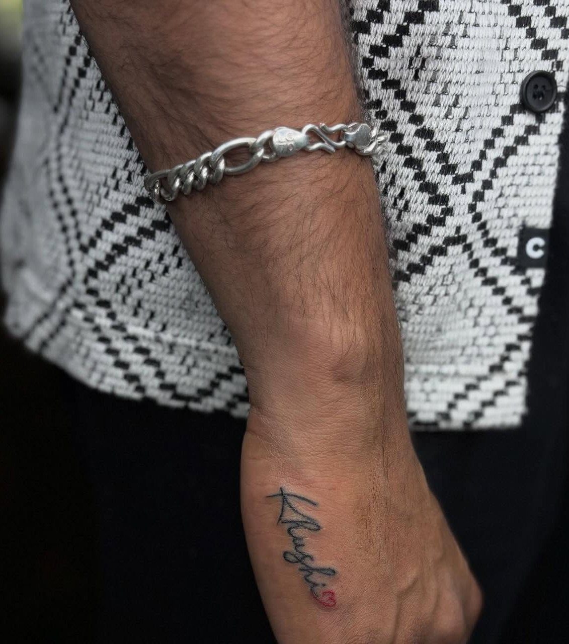 Cursive name tattoo with a red heart on the side of a hand