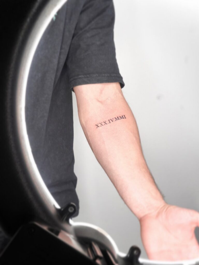 Roman numeral tattoo on a person's inner forearm in black ink.