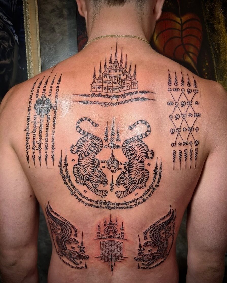 Back of a man with traditional black ink sak yant tattoos including tigers.