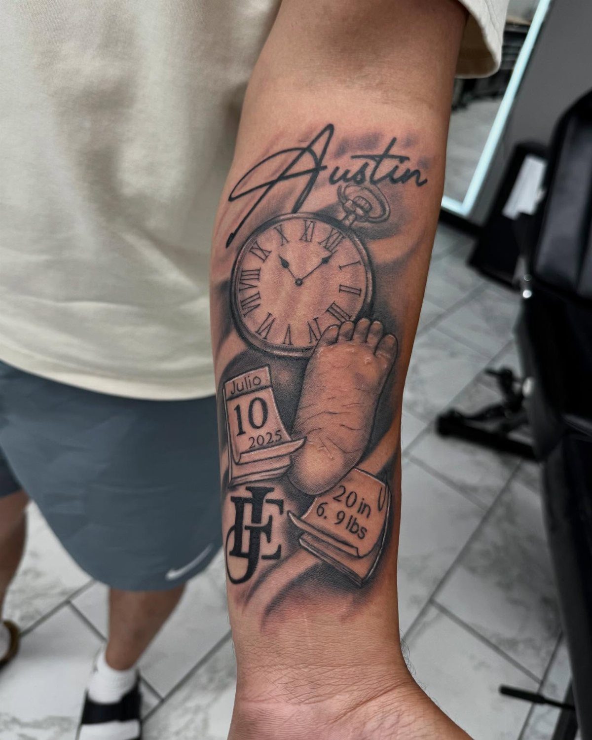 Forearm tattoo featuring a baby footprint, pocket watch, and the name Austin.