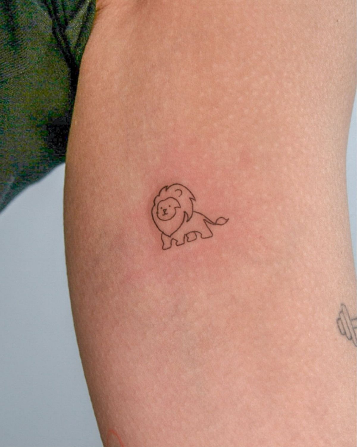 Small minimalist lion line drawing tattoo on a person's arm.