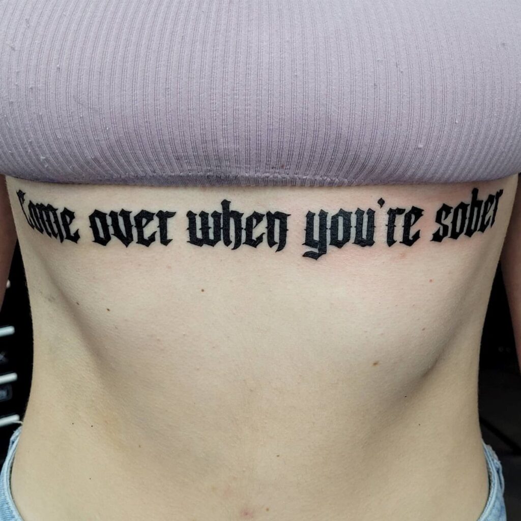 Gothic blackletter tattoo on a person's stomach reading Come over when you're sober
