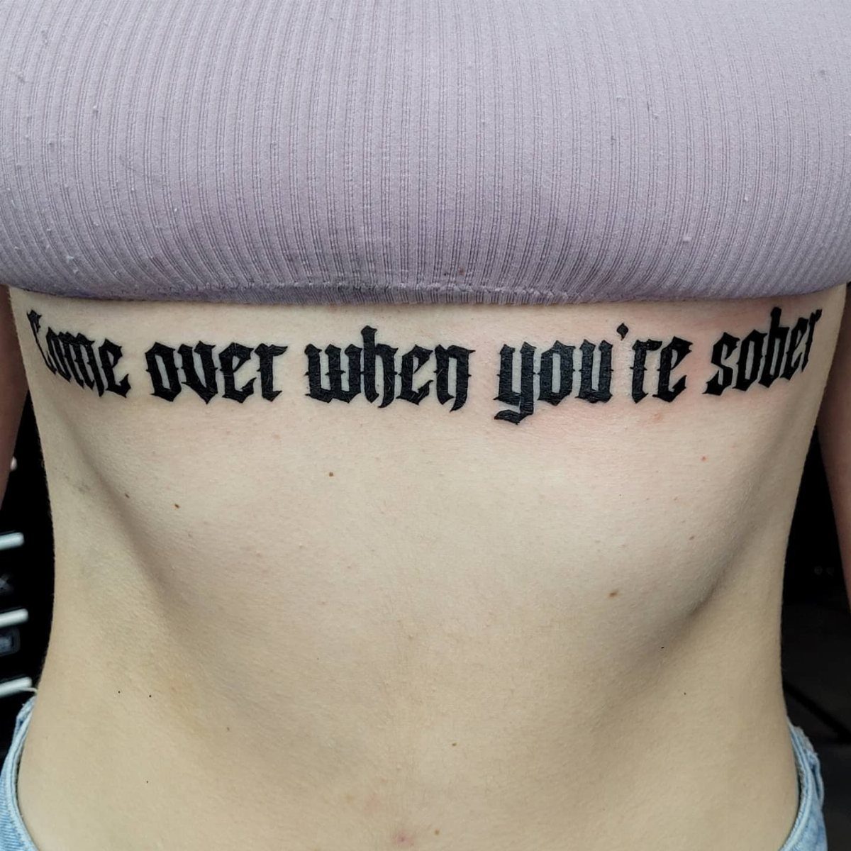 Gothic blackletter tattoo on a person's stomach reading Come over when you're sober