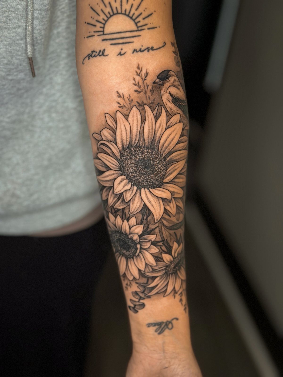 Sunflower tattoo on a forearm with a small bird and a rising sun.