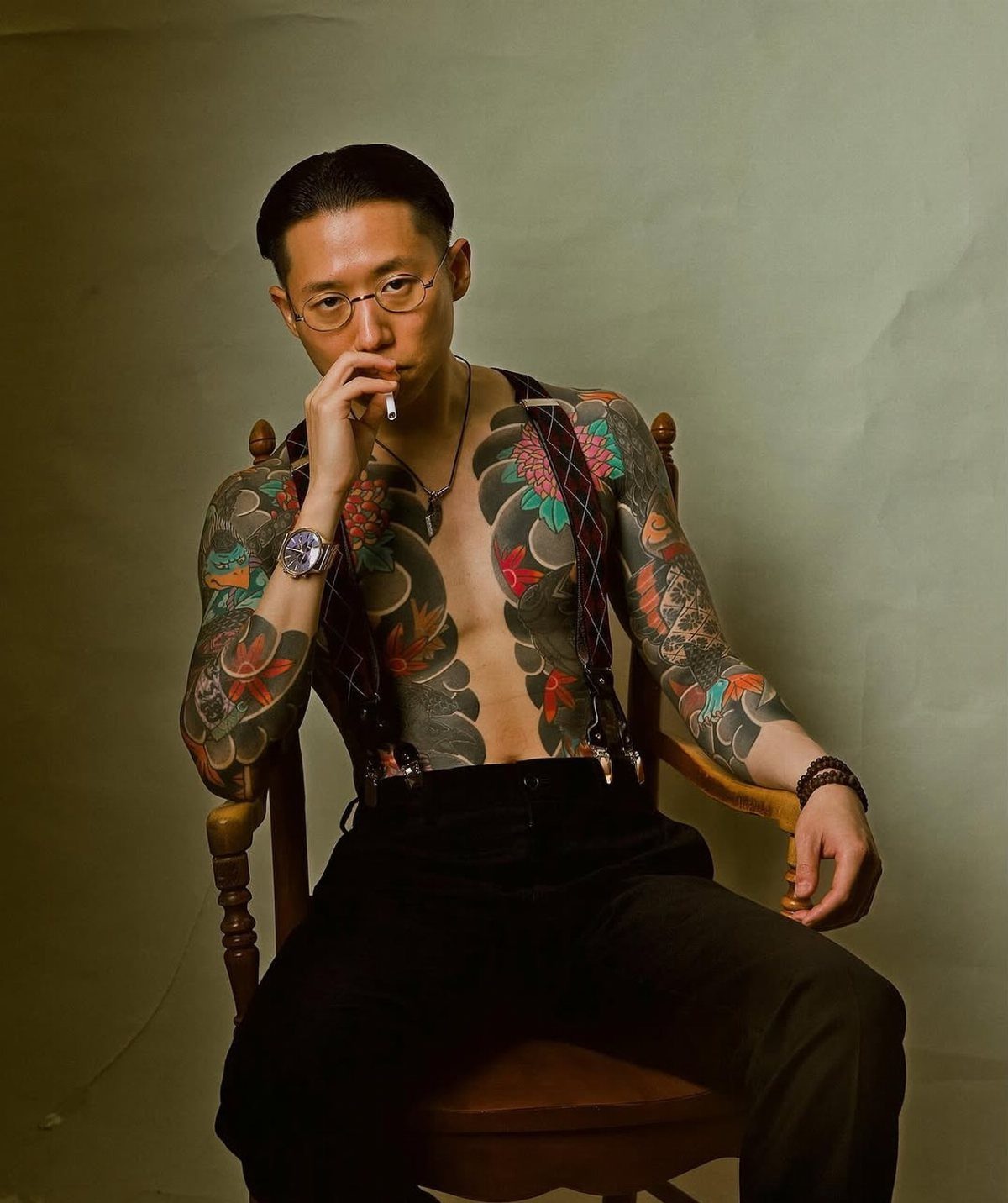 Man with traditional Japanese tattoos on chest and arms sitting in wooden chair