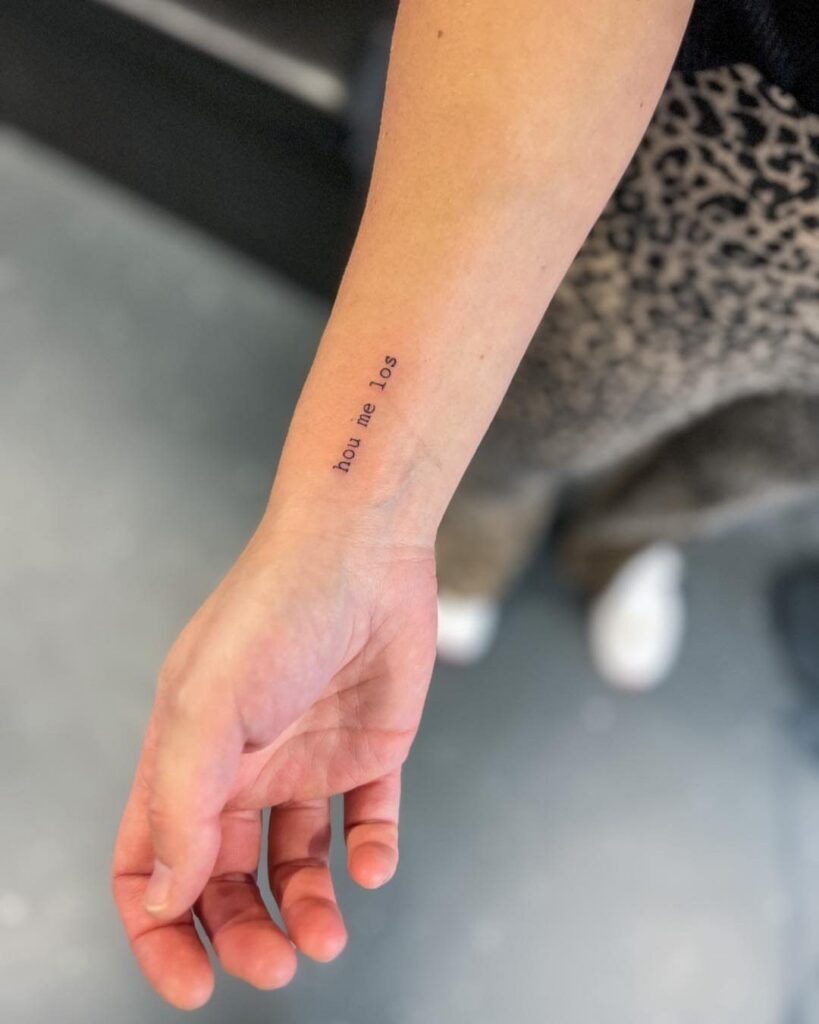Small typewriter font tattoo on a person's inner wrist reading hou me los