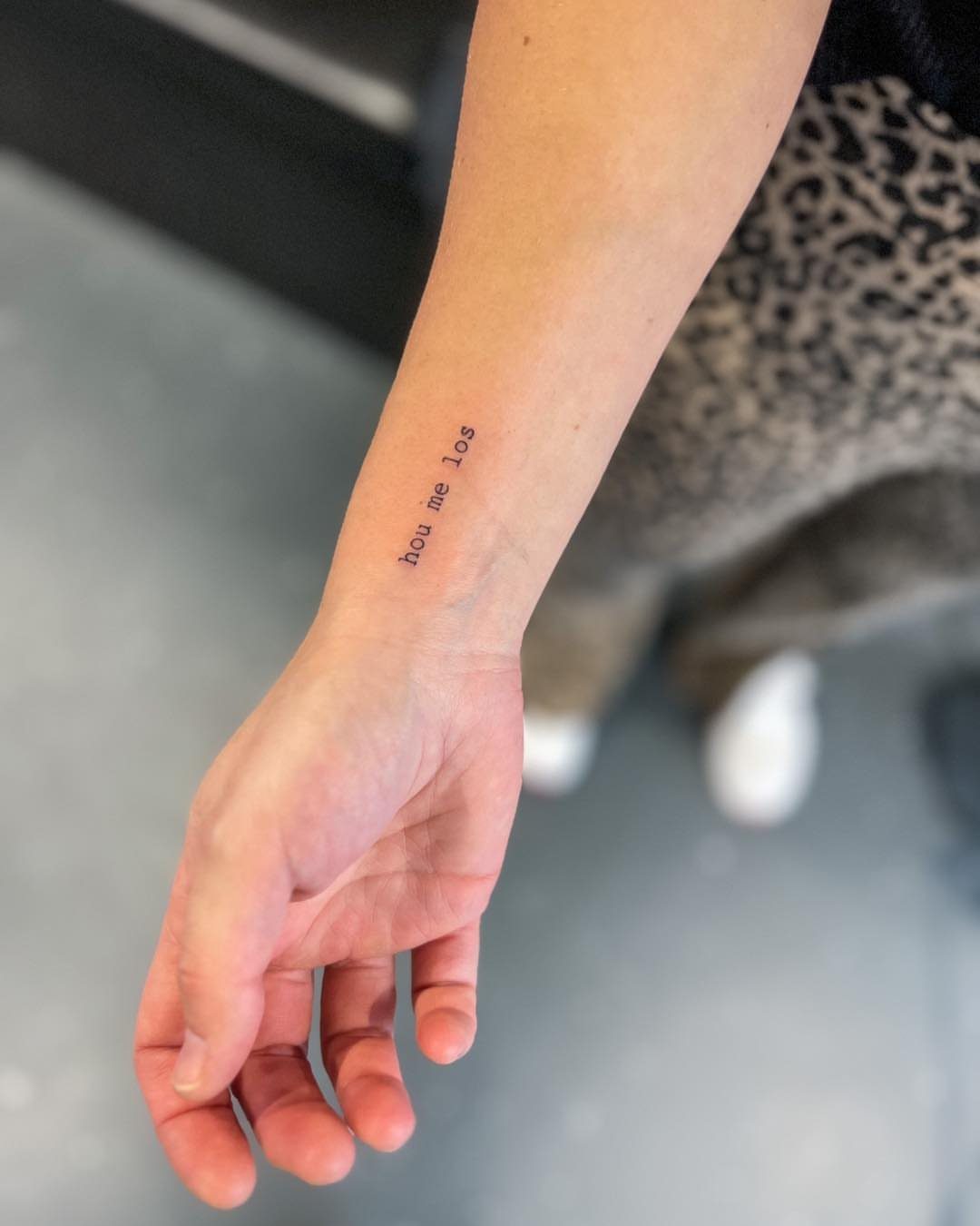 Small typewriter font tattoo on a person's inner wrist reading hou me los