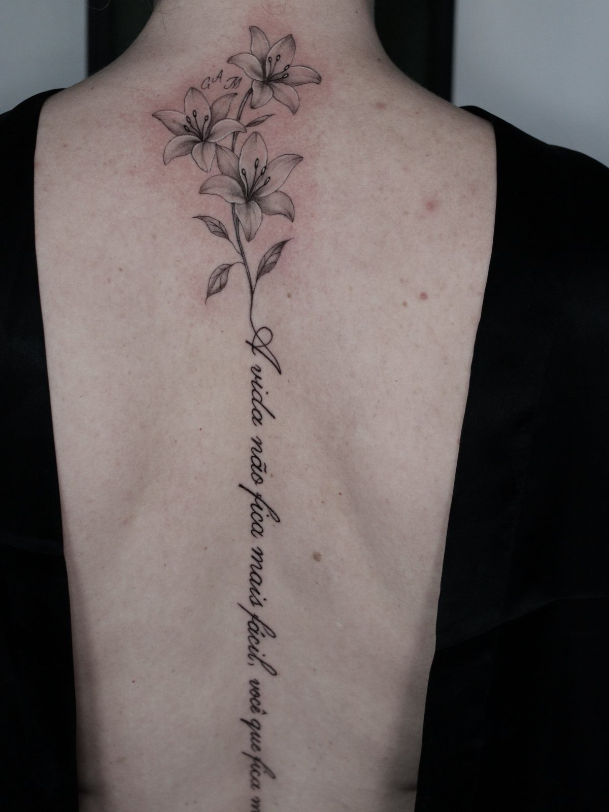 Lily flowers and a long cursive quote tattooed vertically down a person's spine.